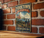 A vintage metal sign with the text "YORKTOWN BATTLEFIELD VIRGINIA" and an illustration of a cannon, two men in military uniforms, and a ship in the background, mounted on a brick wall.