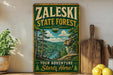 A vintage-style metal sign for the Zaleski State Forest in Ohio, featuring a scenic illustration of a forest landscape with a river and mountains.
