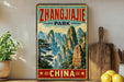 A vintage-style metal sign displaying the text "Zhangjiajie Park" and "China" in a mountainous landscape, with a wooden paddle and a potted plant in the foreground.