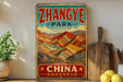 A vintage-style sign for "Zhangye Park" in China, featuring a colorful mountain landscape and the text "Zhangye Park" prominently displayed.