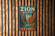 A vintage-style metal sign with the text "ZION NARROWS" and "UTAH" is displayed on a wooden wall.