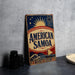 A vintage-style sign for "American Samoa" is displayed on a table, featuring a sun and palm tree design.