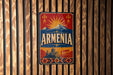 A vintage-style sign with the word "ARMENIA" prominently displayed, featuring a mountain landscape and a sunburst design.