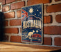 A vintage-style metal sign with the word "AUSTRALIA" prominently displayed, featuring a kangaroo and a red rock formation, all set against a backdrop of stars and a red, white, and blue color scheme.