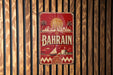 A vintage metal sign with the word "BAHRAIN" prominently displayed, featuring a cityscape and palm trees.