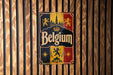 A vintage metal sign with the word "Belgium" prominently displayed, featuring a coat of arms and a castle in the background.