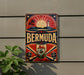 A vintage metal sign with the word "Bermuda" prominently displayed, featuring a sun, lighthouse, and other nautical elements.
