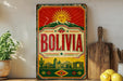 a vintage-style metal sign with the word "BOLIVIA" prominently displayed, along with a sun and mountain motif. The sign is placed on a shelf next to a wooden cutting board and some potted plants, creating a rustic and homey atmosphere.