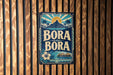 A vintage-style sign with the text "BORA BORA" displayed prominently in the center, surrounded by tropical imagery such as palm trees, a sun, and a mountain.