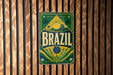 A vintage metal sign with the word "BRAZIL" prominently displayed, featuring a tropical landscape with palm trees and a sun.