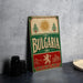 A vintage-style sign for Bulgaria, featuring a sun and floral design, is displayed on a table next to some black camera lenses.
