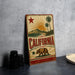 A vintage-style metal sign with the word "CALIFORNIA" prominently displayed, featuring a sun, palm trees, and a bear.