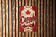 A vintage-style metal sign with the word "Canada" prominently displayed, featuring a maple leaf and a mountain landscape.