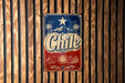 A vintage metal sign with the word "Chile" prominently displayed, featuring a star and palm trees, is mounted on a wooden wall.