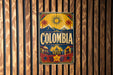 A vintage-style sign with the word "COLOMBIA" prominently displayed, featuring a sun, palm trees, and other tropical elements.