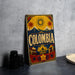 A vintage-style metal sign with the word "COLOMBIA" prominently displayed, featuring a sun, palm trees, and other colorful elements.
