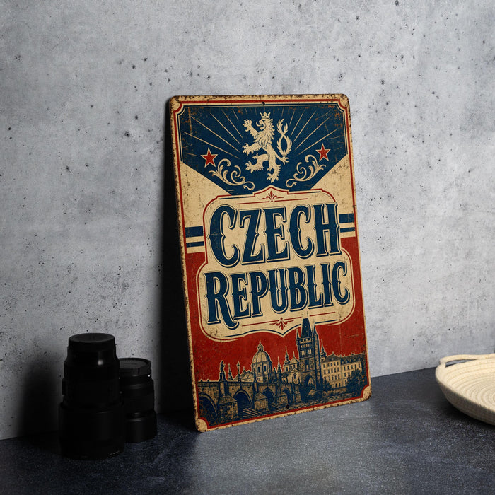 A vintage-style metal sign with the text "Czech Republic" prominently displayed, featuring a lion and a castle-like structure. The sign is placed on a gray surface, with some black camera lenses visible in the background.