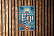 A vintage-style metal sign with the word "Fiji" prominently displayed, featuring palm trees, a hibiscus flower, and a sailboat.