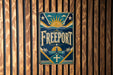 A vintage metal sign with the word "FREEPORT" displayed prominently in the center, surrounded by various decorative elements such as a sun, palm trees, and stars.