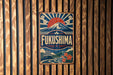 a vintage-style sign with the word "FukUSHIMA" prominently displayed, surrounded by a mountain landscape and a sunburst design.