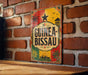 A vintage-style sign for Guineau Bissau beer is displayed on a brick wall.