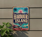 A vintage-style sign for Harbour Island, featuring a sun, palm trees, and a sailboat, mounted on a wall.