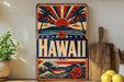 A vintage-style metal sign with the word "HAWAII" prominently displayed, featuring a sunburst design, palm trees, and a wave. The sign is placed on a shelf next to a wooden cutting board and some potted plants.