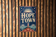 A vintage-style sign that reads "HOPE TOWN" is displayed against a wooden background.