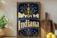 A vintage-style metal sign with the word "Indiana" prominently displayed, featuring a city skyline silhouette and a torch-like symbol. The sign is placed on a shelf next to a wooden cutting board and a potted plant.