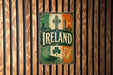 A vintage-style sign with the word "IRLAND" prominently displayed, featuring various Irish symbols and landmarks such as a castle, harp, and shamrock.