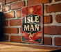 A vintage-style sign with the text "ISLE OF MAN" displayed prominently on a brick wall.