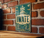 A vintage-style sign with the word "IWATE" prominently displayed, mounted on a brick wall.