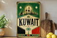 a vintage-style sign with the word "KUWAIT" prominently displayed, surrounded by a green and red border. The sign is placed on a shelf next to a wooden cutting board and a potted plant, creating a homely and inviting atmosphere.