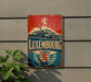 A vintage metal sign with the word "LUXEMBOURG" prominently displayed, featuring a castle, lion, and laurel wreath design.