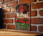 A vintage metal sign with the word "Malawi" displayed prominently, featuring a sun-like design and a landscape with a tree and mountains.