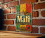 A vintage metal sign with a colorful design and the word "Mali" prominently displayed, mounted on a brick wall.