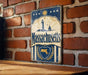 A vintage metal sign displaying the name "Massachusetts" with a lighthouse and sailboat illustration, mounted on a brick wall.