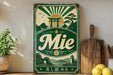 A vintage-style sign with a green and white color scheme, featuring a Japanese-inspired design with a torii gate, mountains, and a sun. The sign displays the word "Mie" prominently in the center.