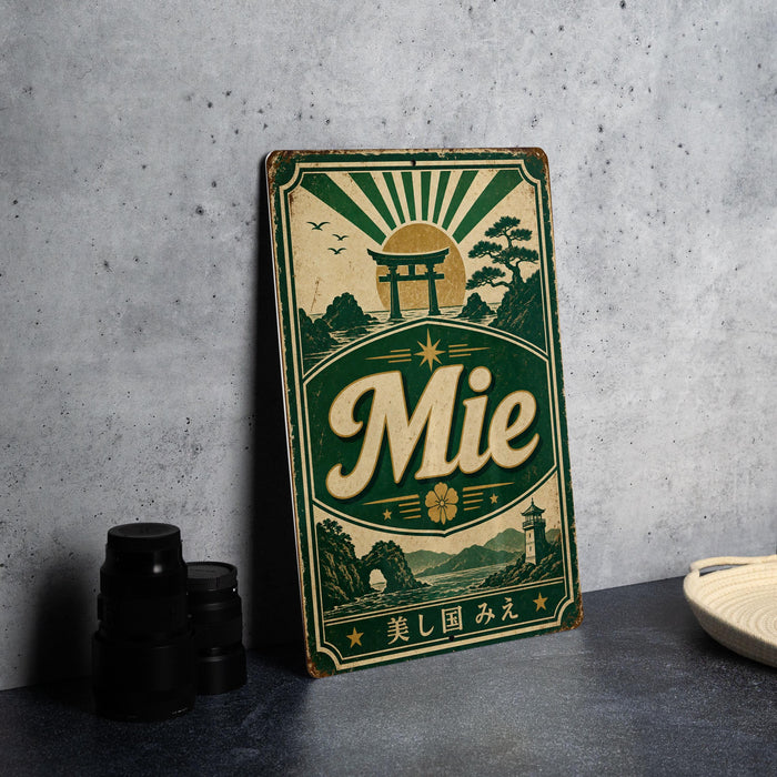 A vintage metal sign with a green and gold design, featuring a Japanese-style torii gate and mountains, along with the word "Mie" prominently displayed.