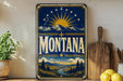A vintage-style metal sign with the word "Montana" prominently displayed, featuring a sun and mountain landscape design.