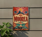 a vintage-style sign with a tropical design, hanging on a wall next to a plant.