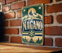 A vintage-style sign with the word "NAGANO" prominently displayed, featuring a mountain landscape and snowflake design.