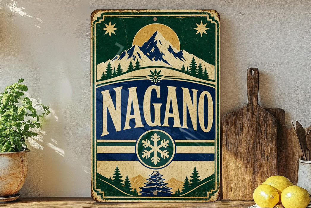 A vintage-style sign with the word "NAGANO" prominently displayed, featuring a mountain landscape and snowflake design. The sign is placed on a wooden surface, with a potted plant, a wooden cutting board, and some lemons nearby.