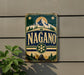 A vintage-style metal sign with the word "NAGANO" prominently displayed, featuring a mountain landscape and snowflake design.