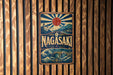 A vintage-style metal sign with the word "Nagasaki" prominently displayed, featuring a sun and waves in the background.