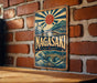 A vintage-style metal sign with a sun and wave design hangs on a brick wall.