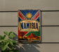 a colorful vintage Namibia sign mounted on a wall, with a plant to the left side.