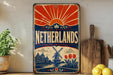 A vintage-style metal sign with the text "Netherlands" prominently displayed, featuring a sunburst design and illustrations of tulips, windmills, and a cityscape.