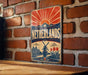 A vintage-style sign for the Netherlands, featuring a sunburst design and a depiction of tulips, is mounted on a brick wall.