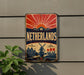 A vintage-style sign with the word "Netherlands" prominently displayed, featuring a sunburst design and a depiction of a windmill and tulips.